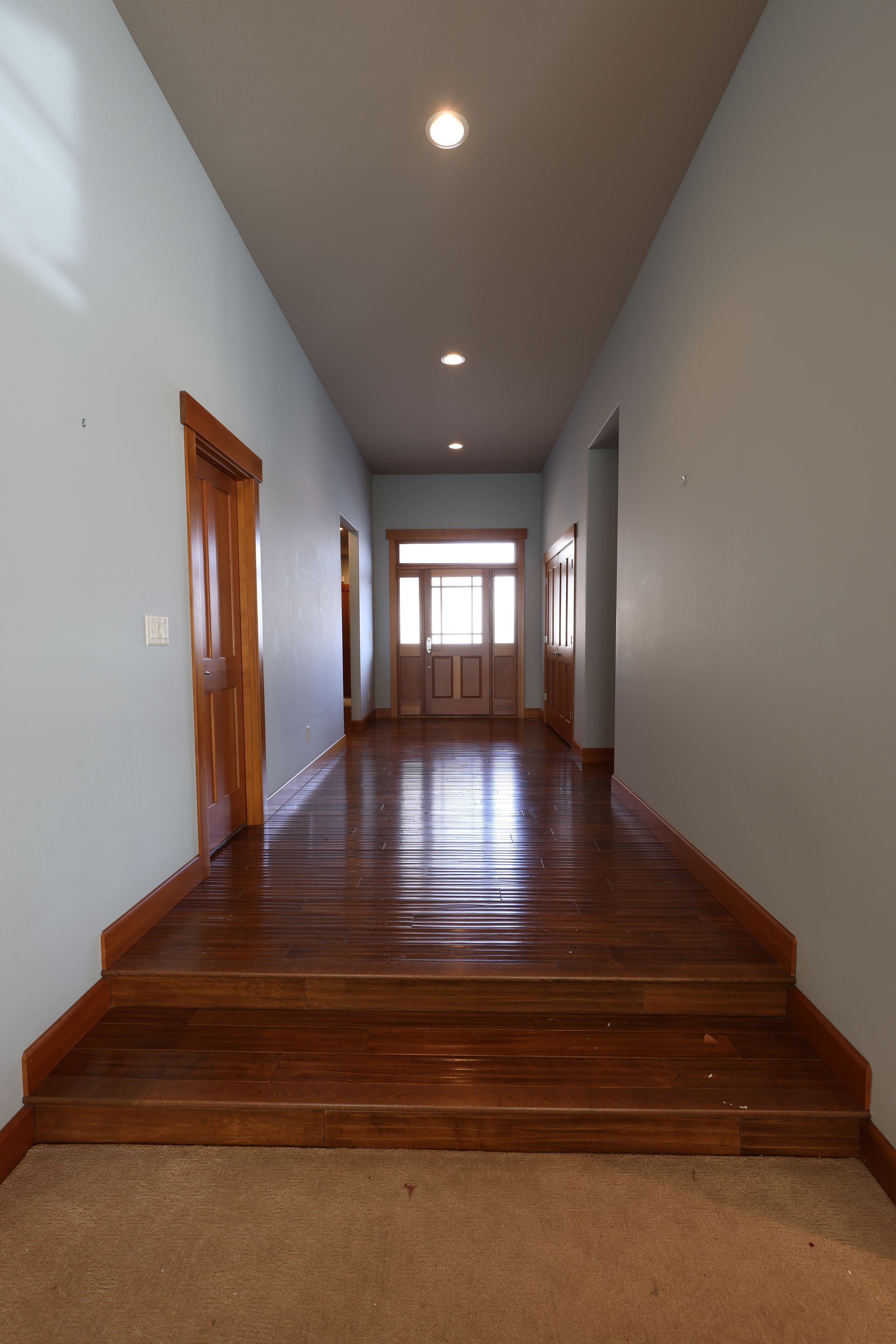 Long hallway with light blue walls, wooden floors, and a door at the end.