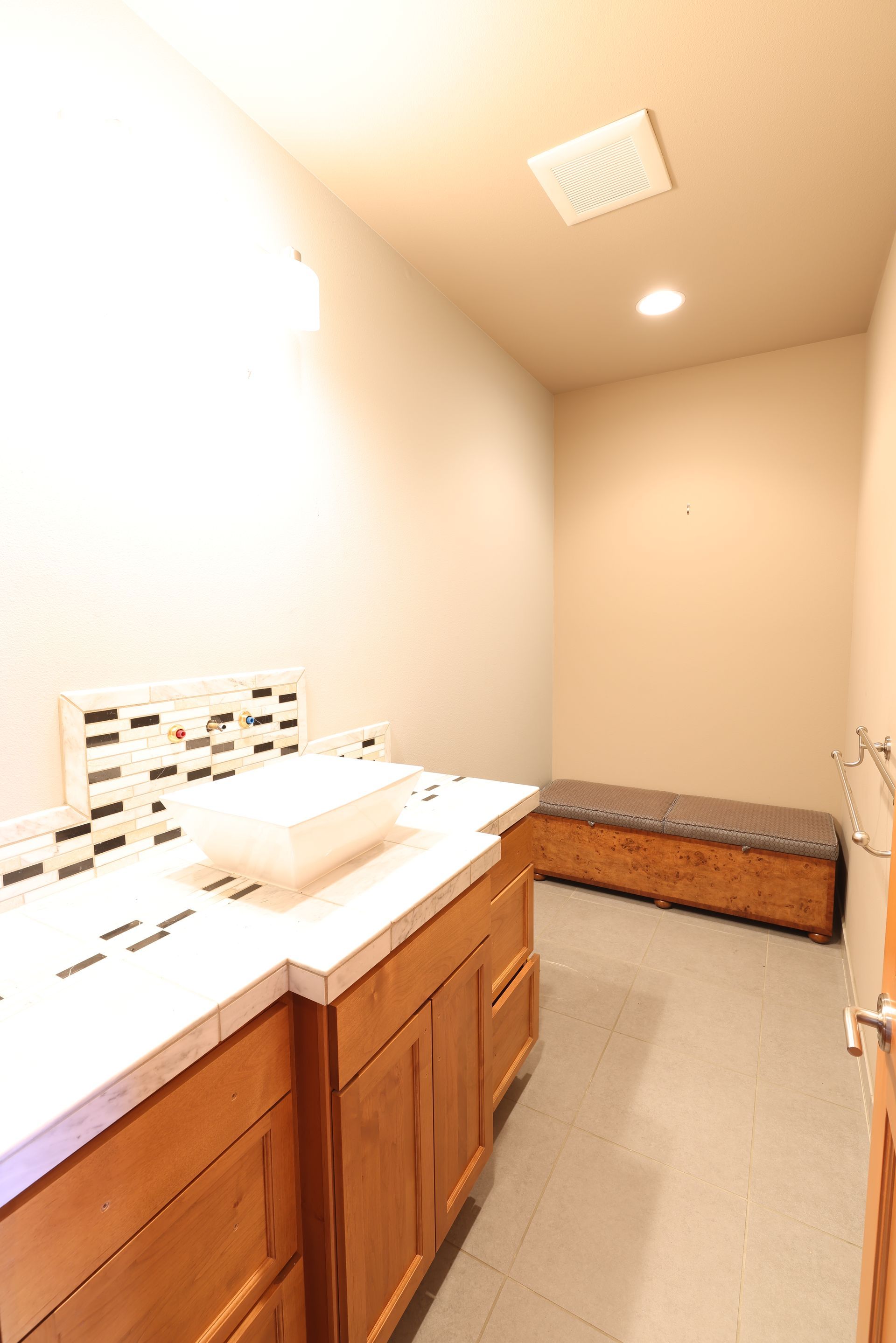 Bathroom with wooden vanity, white countertop, decorative backsplash, and bench.