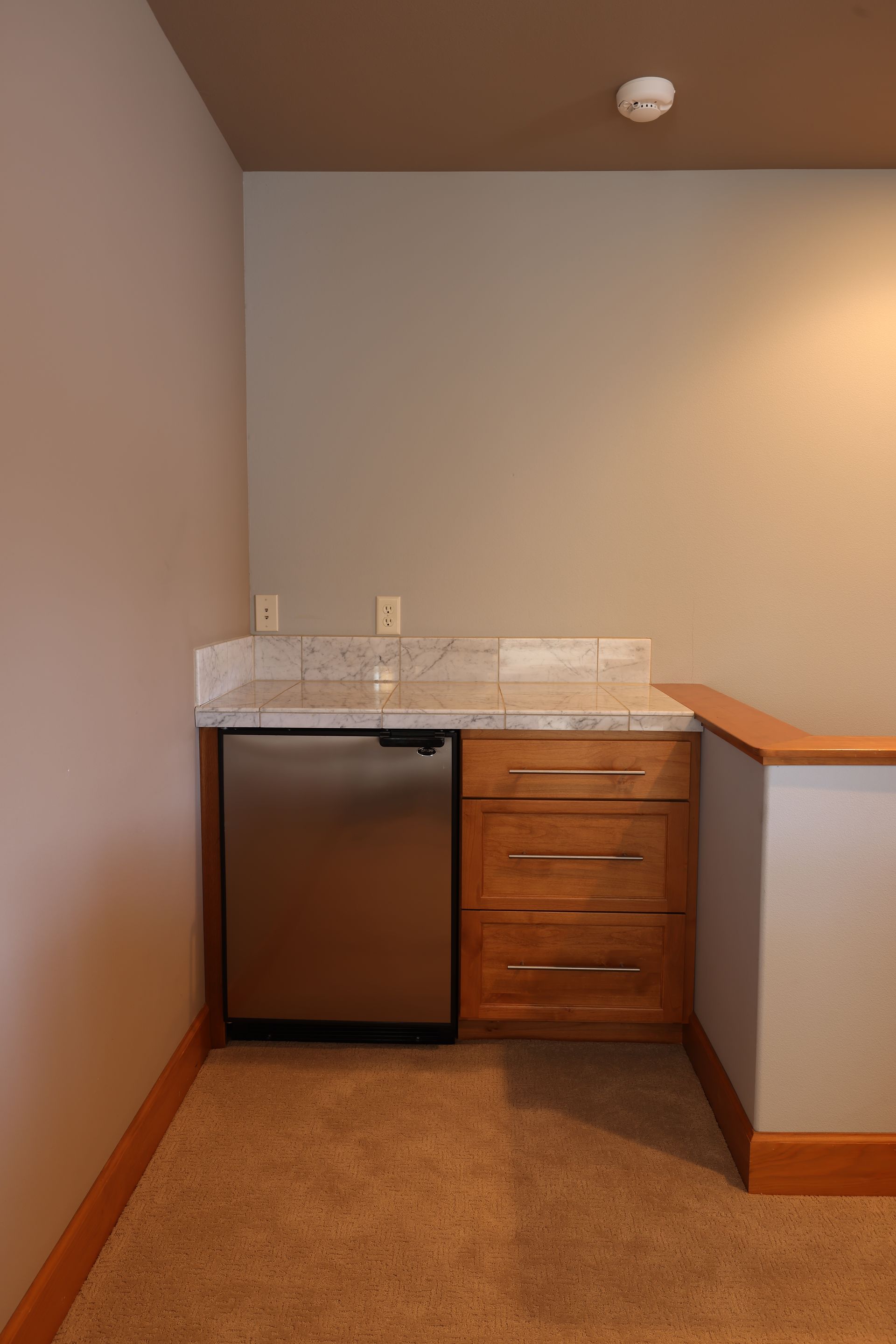 A stainless steel refrigerator and wooden drawers built into a wall with granite countertop.