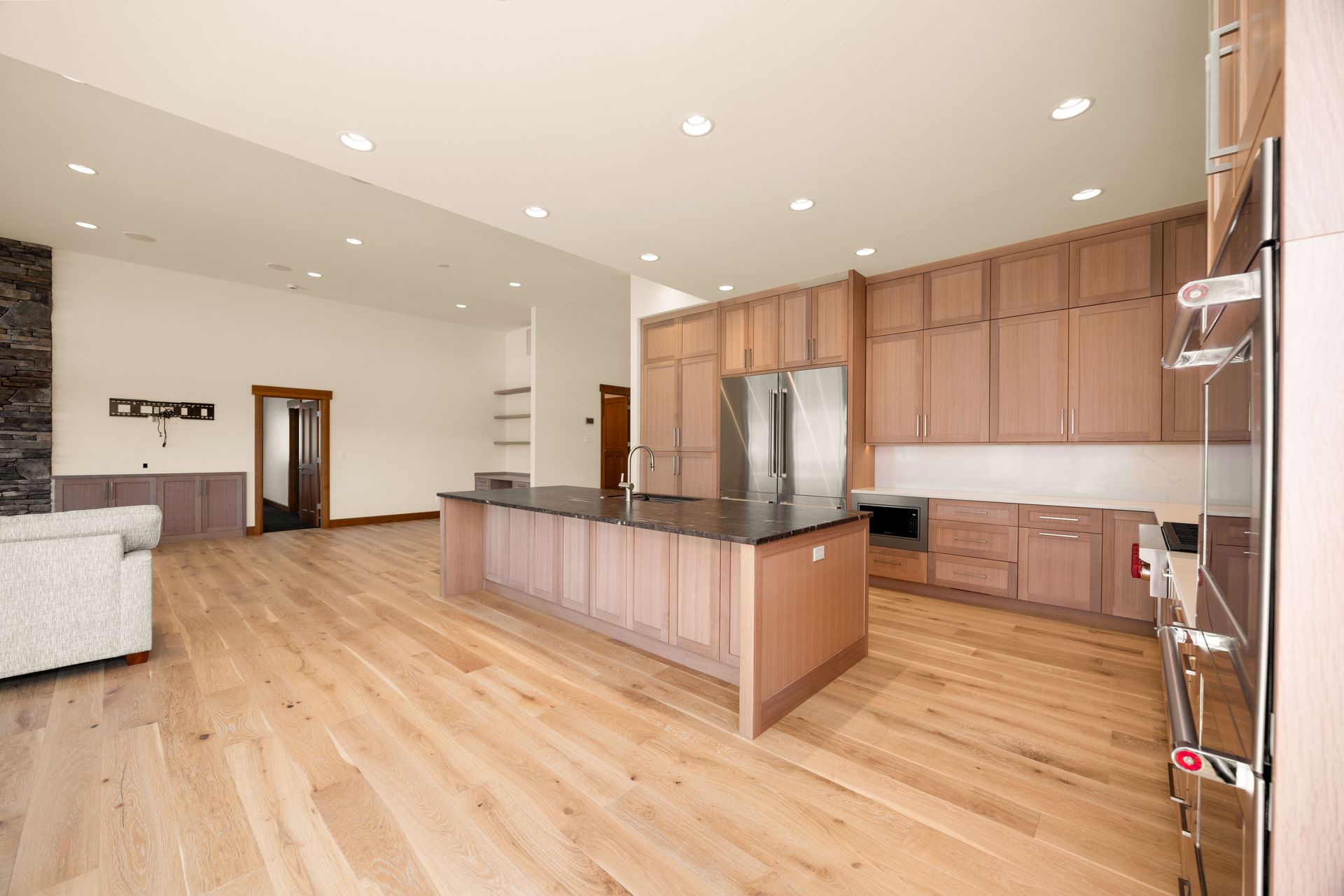 Spacious kitchen with wood cabinets, island, and stainless steel appliances. Open to a large living area with wood floors.