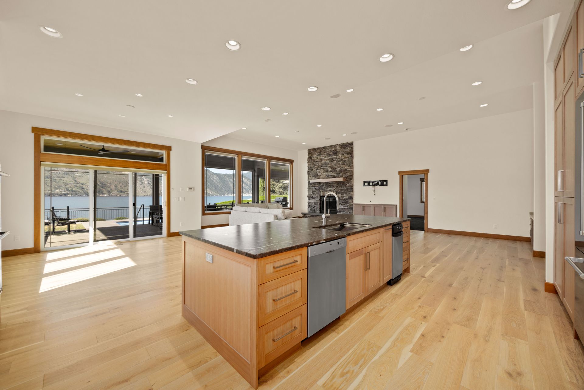 Spacious kitchen with wood floors, island with sink, and sliding glass doors to a deck overlooking water.
