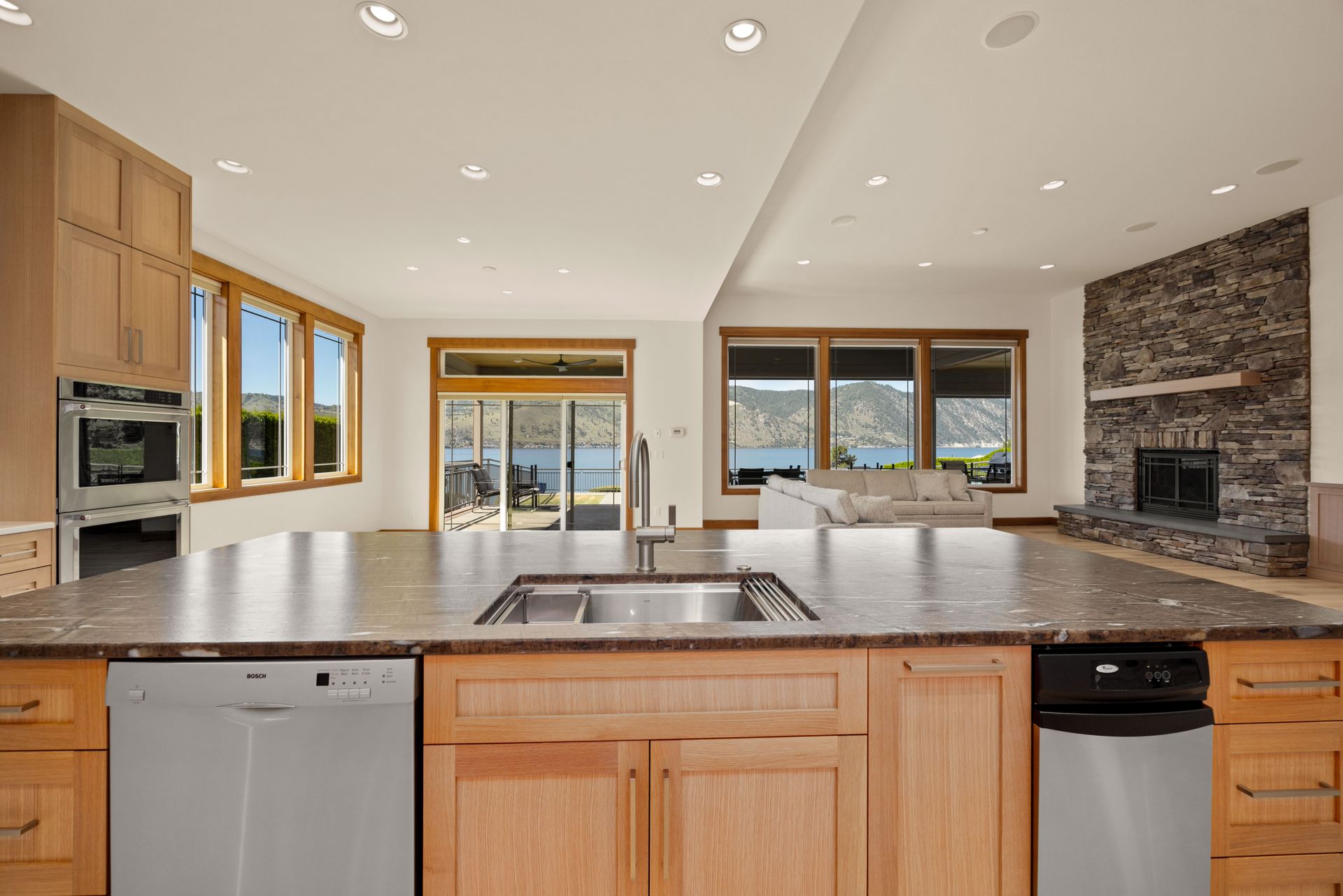 Spacious kitchen with island, sink, and appliances. View of lake through windows and fireplace.