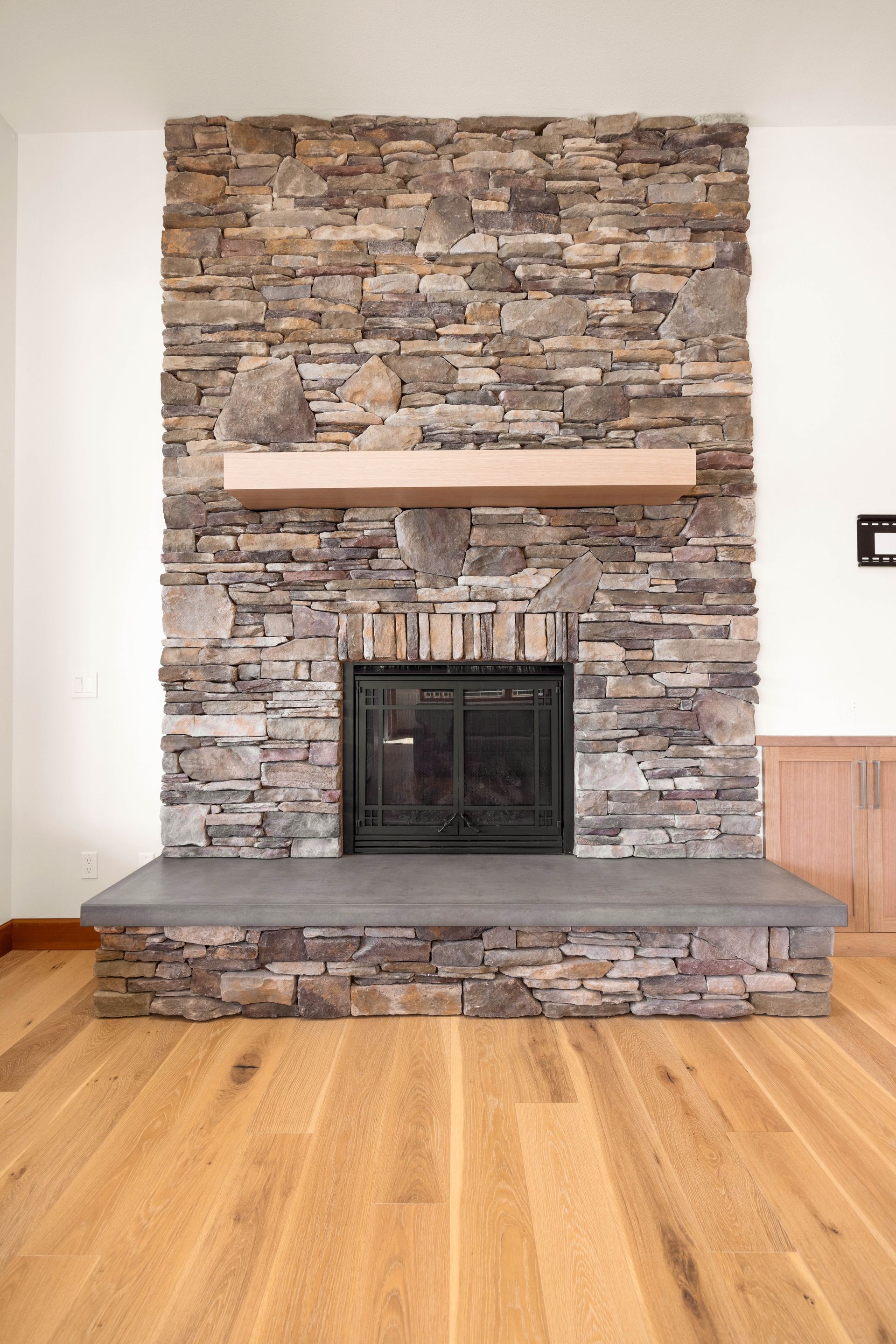 Stone fireplace with gray hearth and wood mantle, set against a white wall and wood floor.