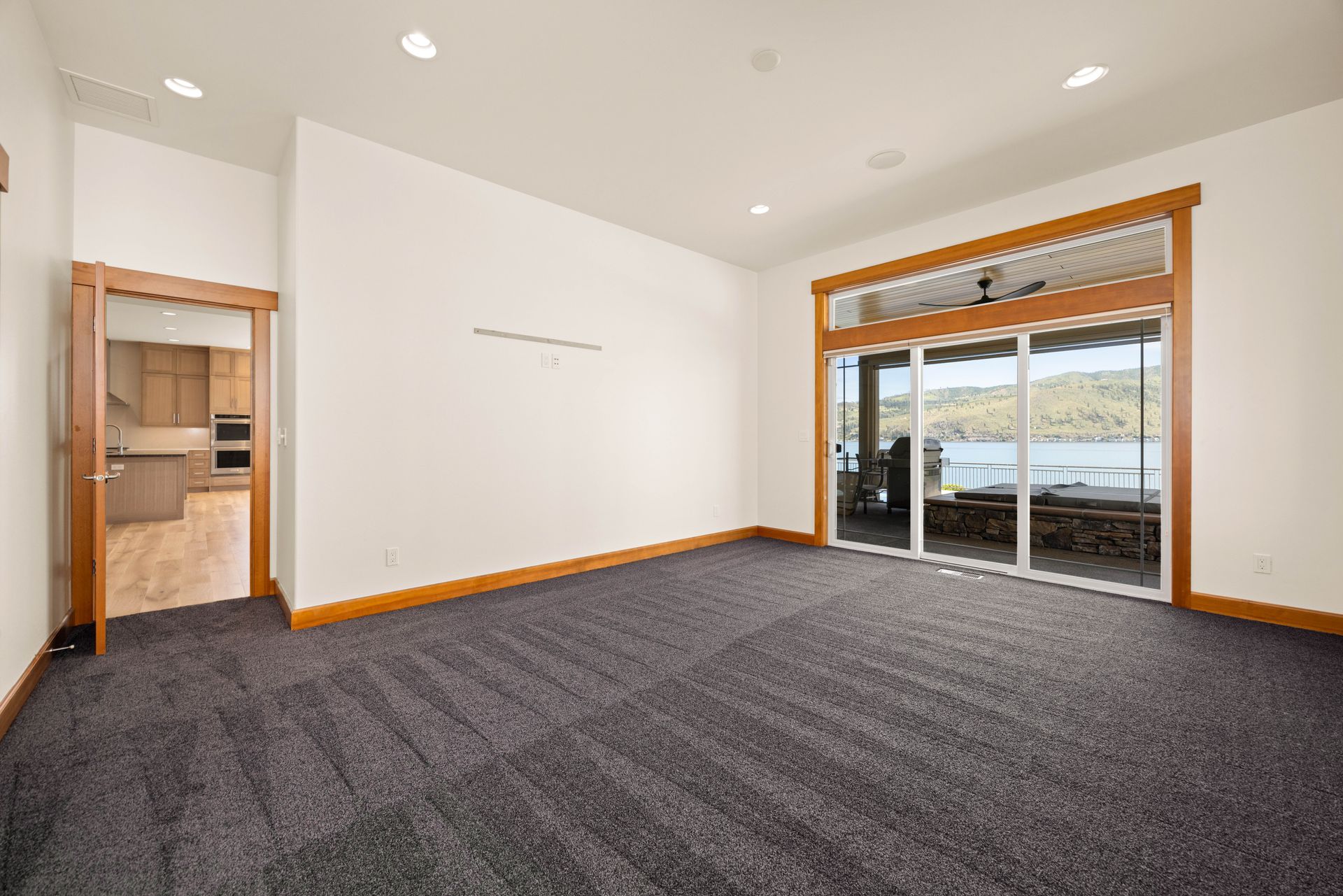 Empty room with gray carpet, sliding glass door with a lake view, and door to a kitchen.