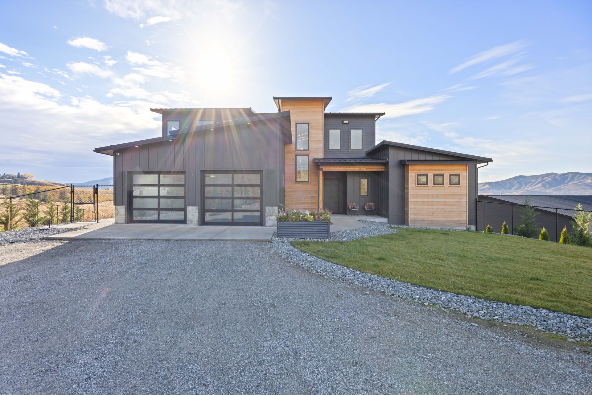 Modern home with gray siding, glass garage doors, and gravel driveway.