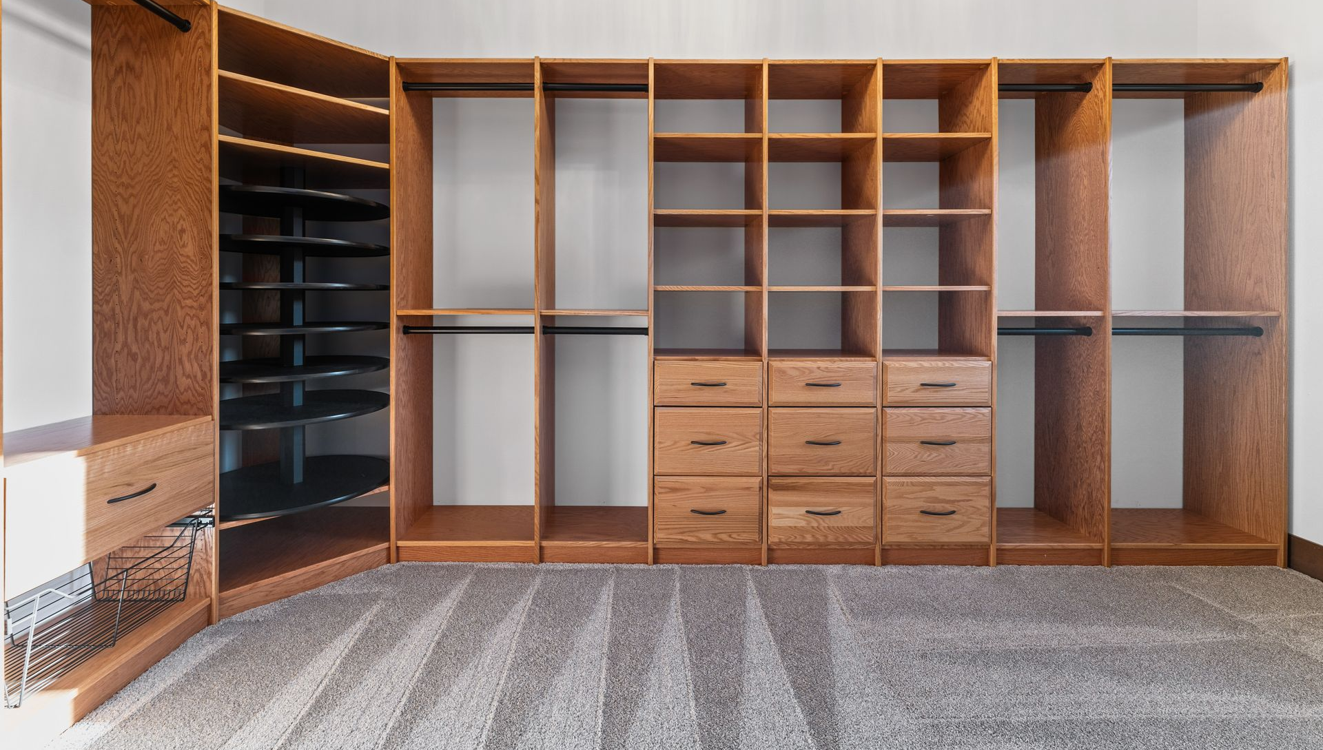 Wooden custom closet with shelves, drawers, and hanging rods, on a gray carpet.