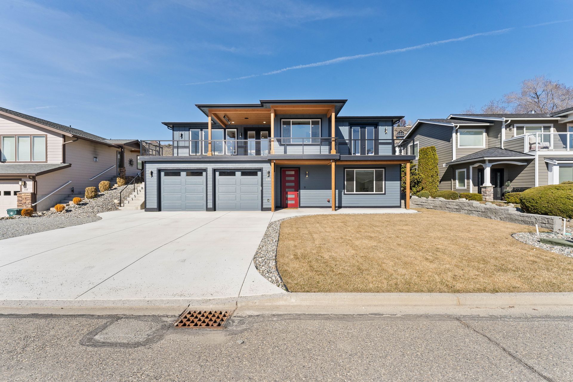 Modern two-story house with gray exterior, red front door, and three-car garage. Sunny day with blue sky.