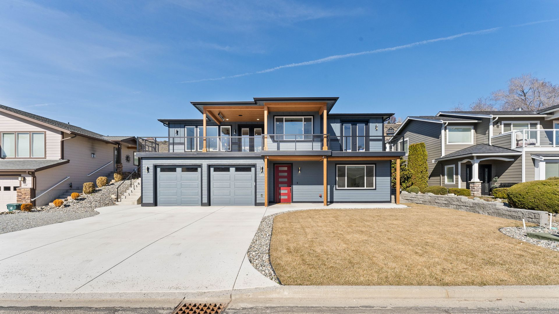 Two-story modern house with gray siding, red door, and a concrete driveway on a sunny day.