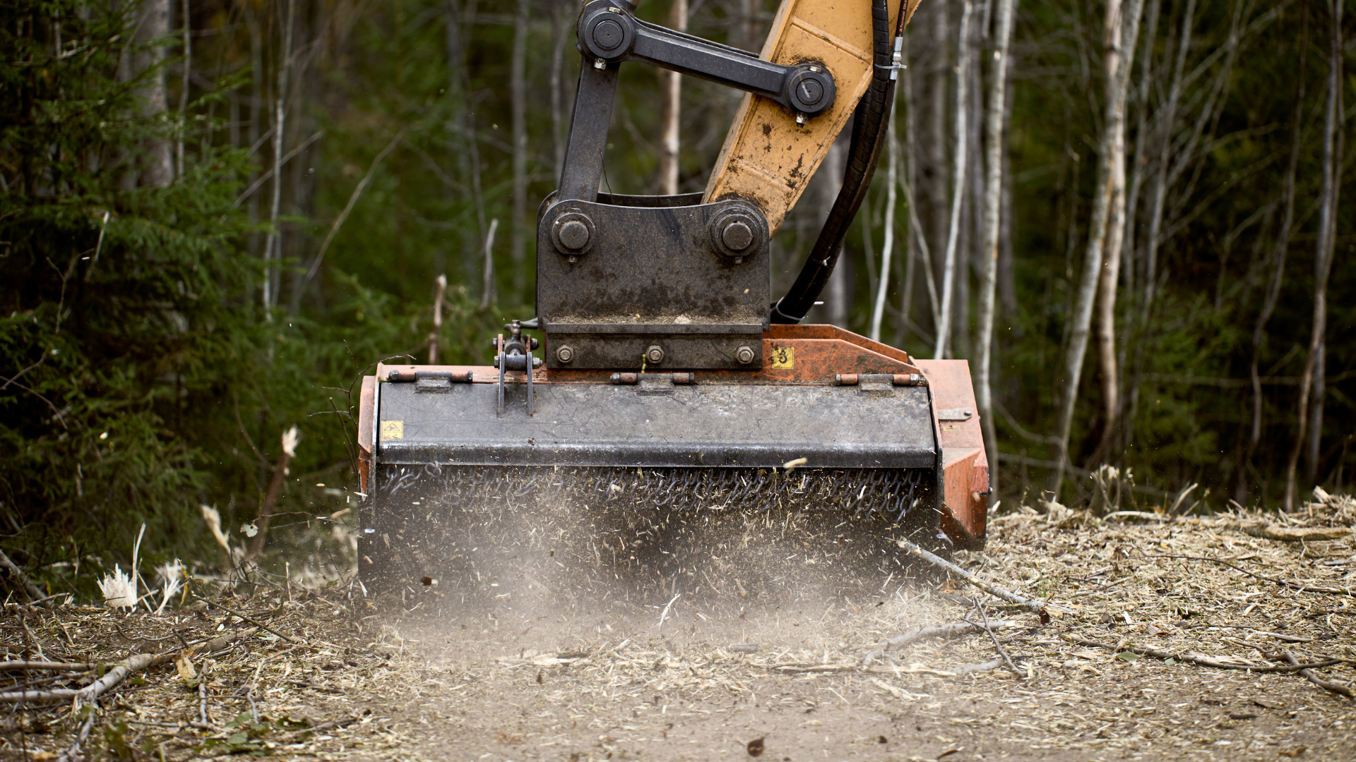 Excavator blade scraping dirt and dust on a forest trail