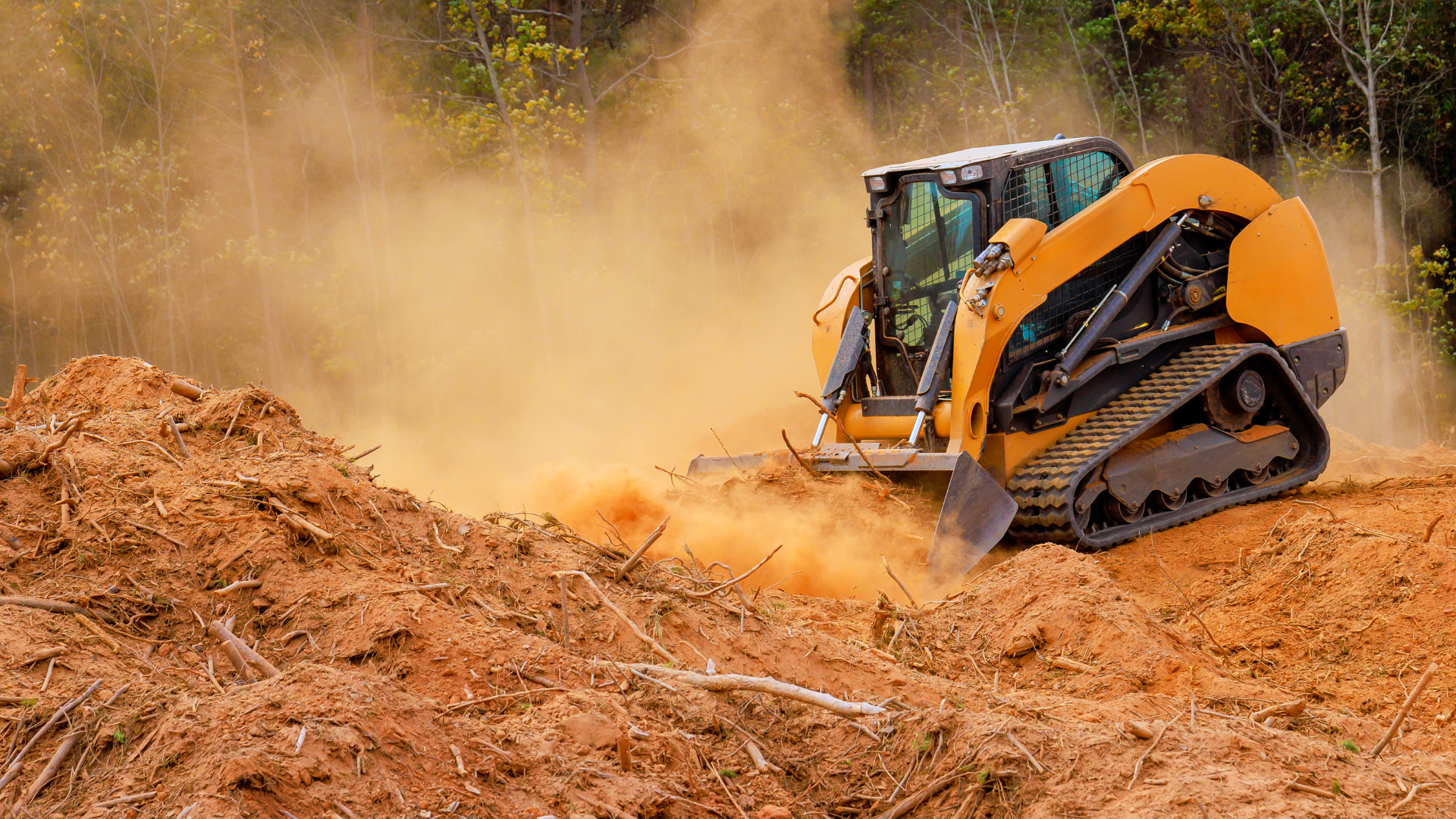 Orange compact loader clearing dirt on a dusty construction site