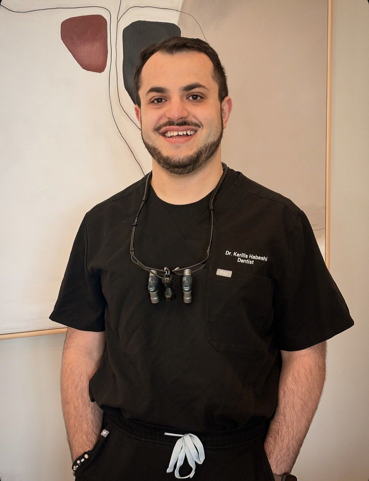 Person smiling in a black T-shirt, standing indoors with glasses hanging from the neck.