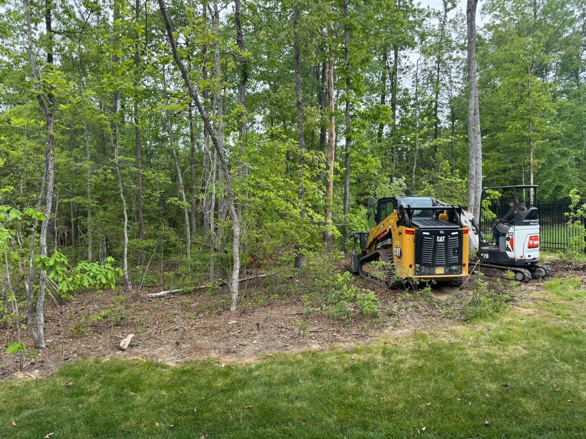 Yellow excavator and white truck parked by a wooded clearing with fresh ground work.