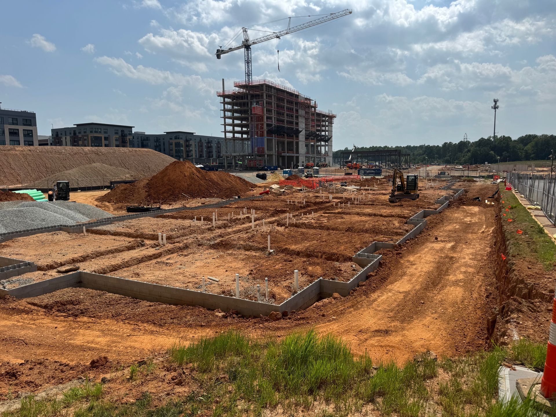 Construction site with foundation trenches, earth piles, and a crane beside a partially built structure