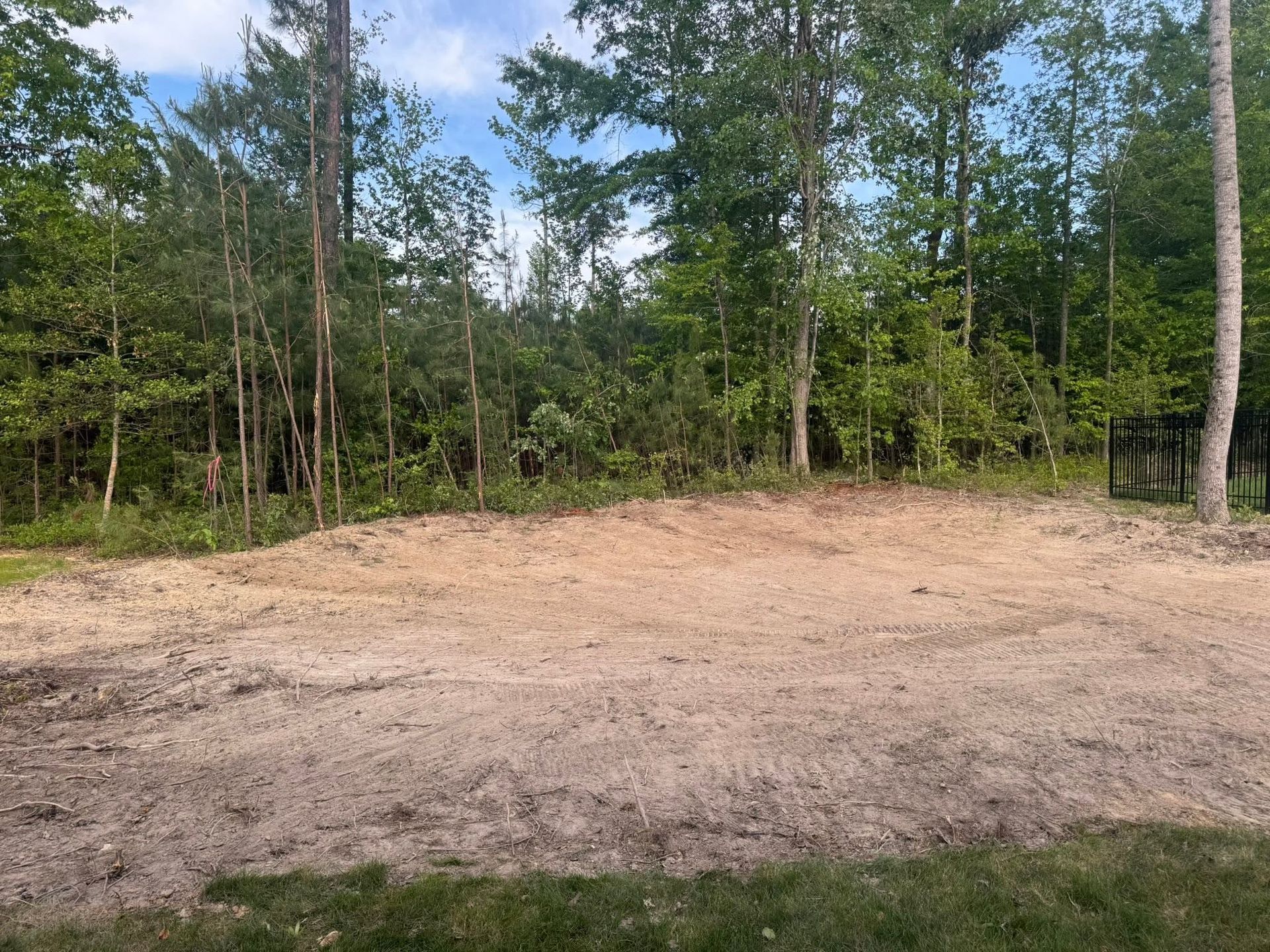 Cleared dirt lot beside a wooded forest with trees and blue sky in the background