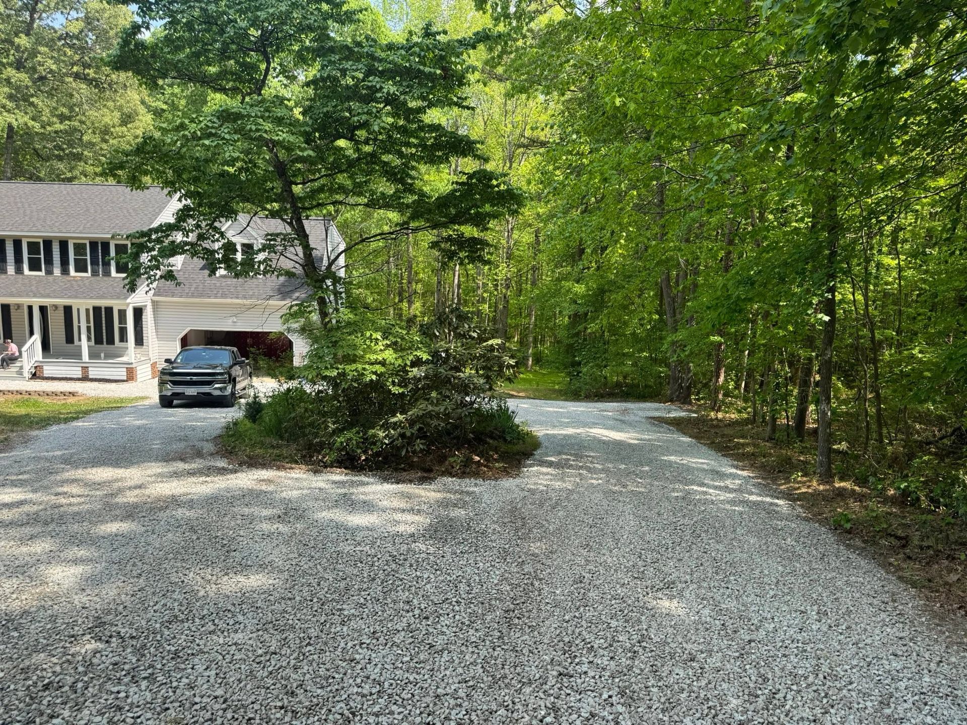 Gravel driveway leading to a house with a parked SUV, surrounded by green trees.