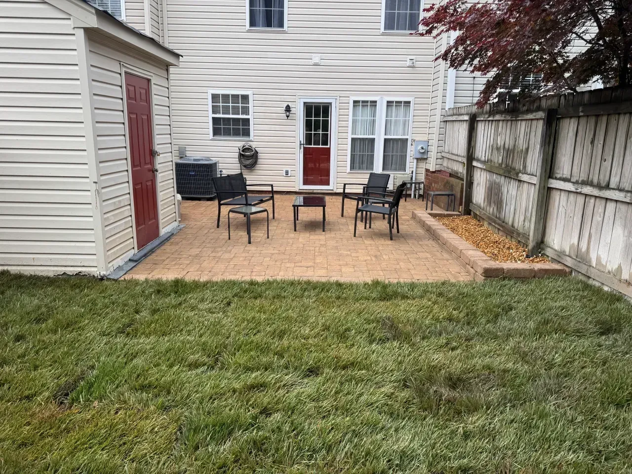 Backyard patio with chairs, table, grill, and red door beside a fenced lawn