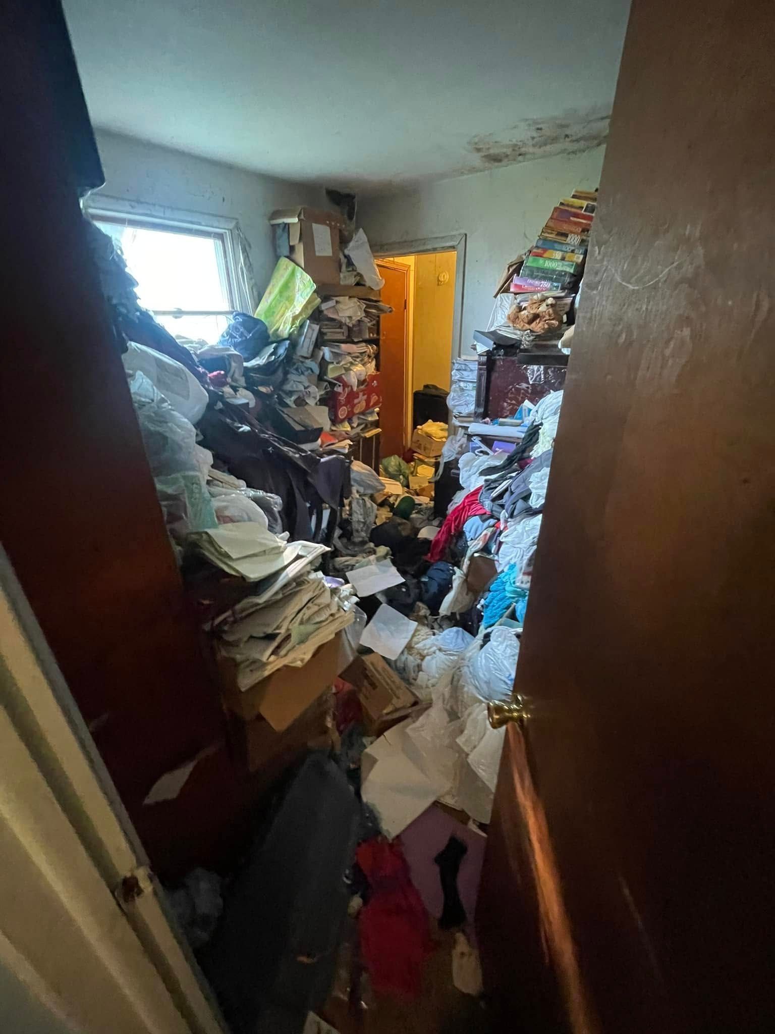 A view through a doorway into a room filled with piles of clutter, scattered papers, and items covering the floor.