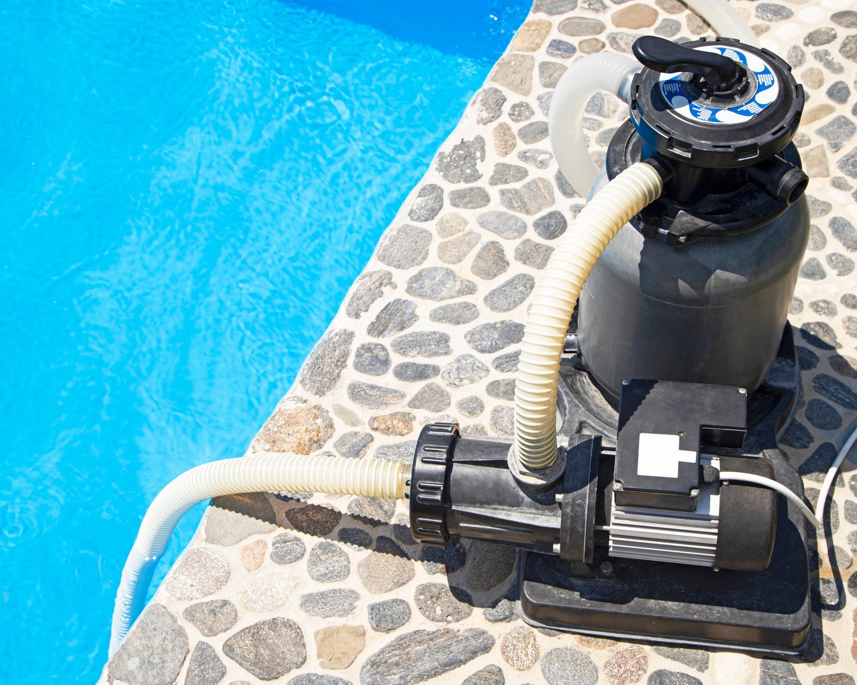 A pool filter is sitting on the edge of a swimming pool. A pool filter is sitting on the edge of a swimming pool.