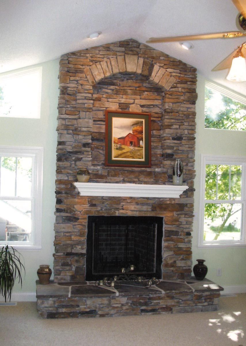 Stone fireplace with an arched top, a painting, and white mantle, flanked by windows.