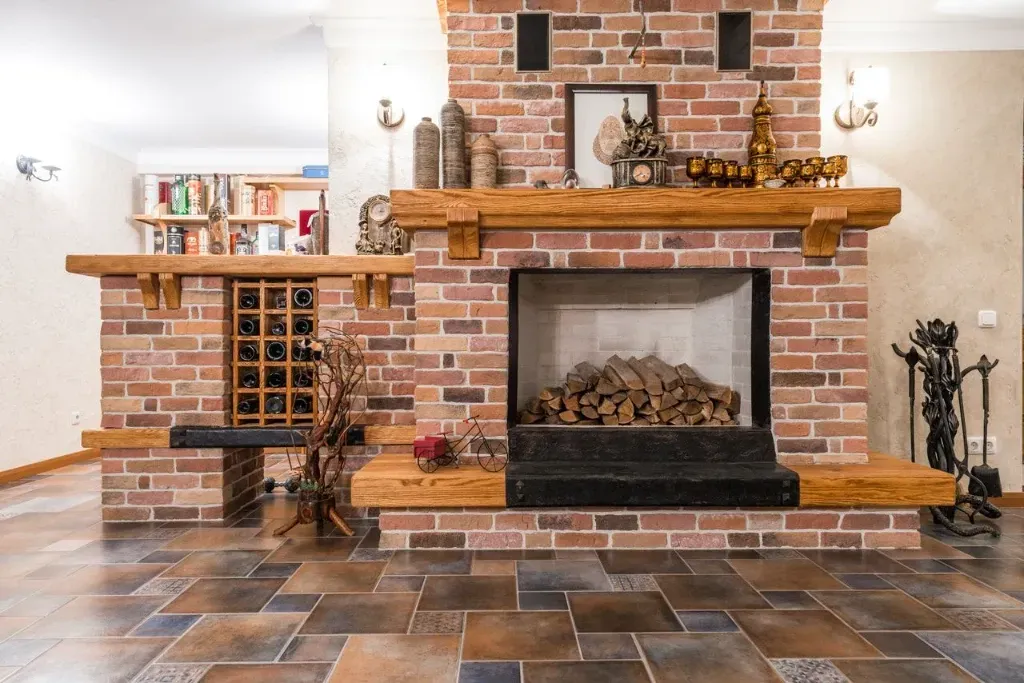 Brick fireplace with wooden mantel, built-in wine rack, and dark tiled floor in a cozy living room