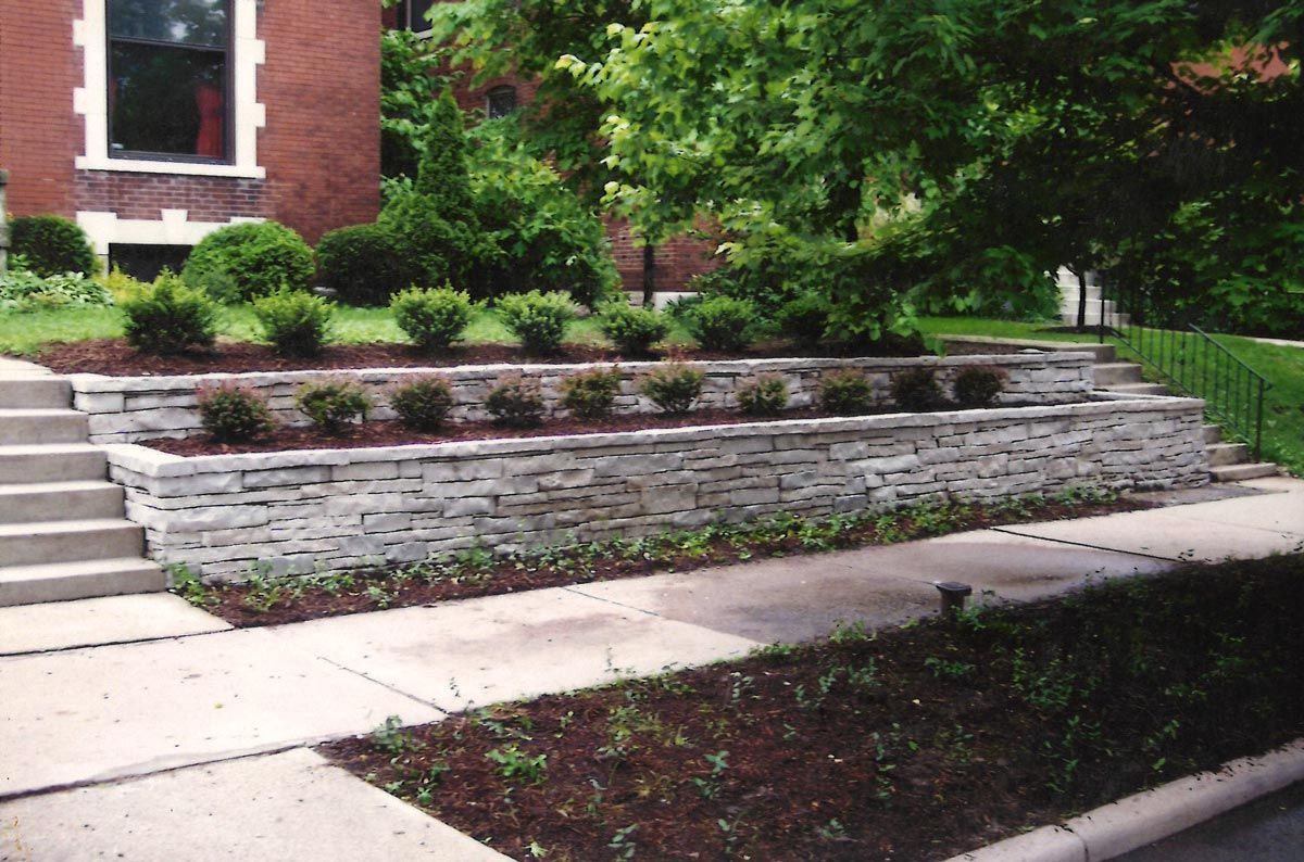 Stone retaining wall with a landscaped garden in front of a brick building.