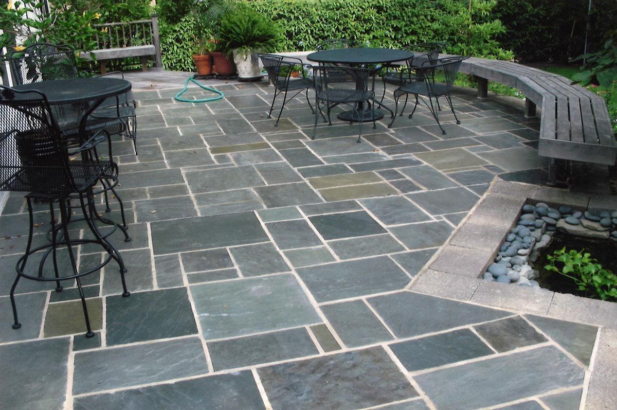 Stone patio with black metal tables and chairs, bench, and plants.