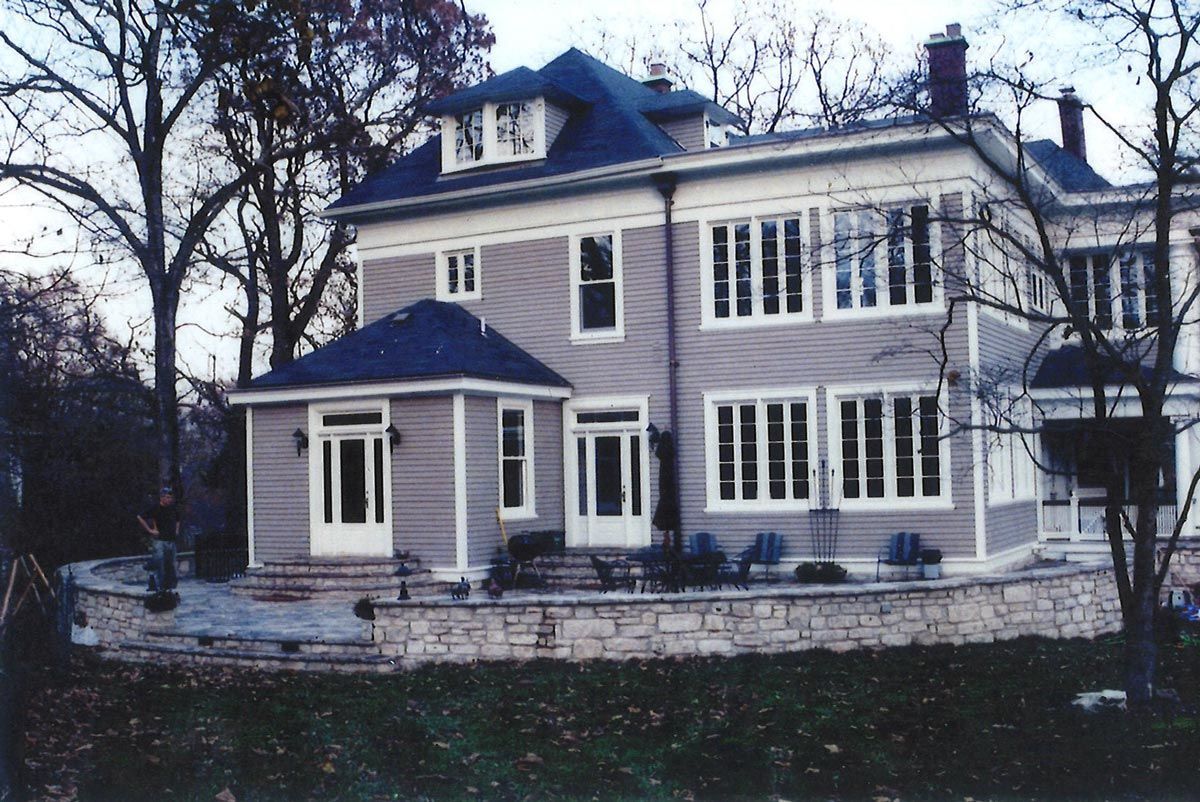 Two-story house with gray siding, white trim, and a stone retaining wall.