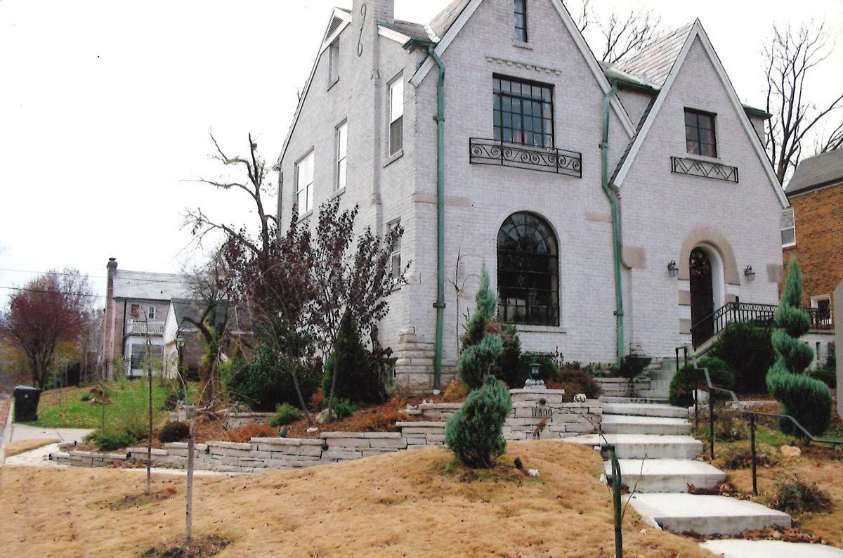 White stucco house with gabled roof, arched windows, and stone steps leading to the front door.