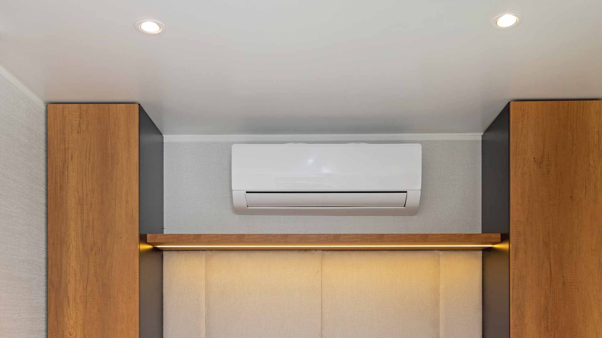 Wall-mounted white air conditioner above a wooden shelf between two cabinets in a modern room
