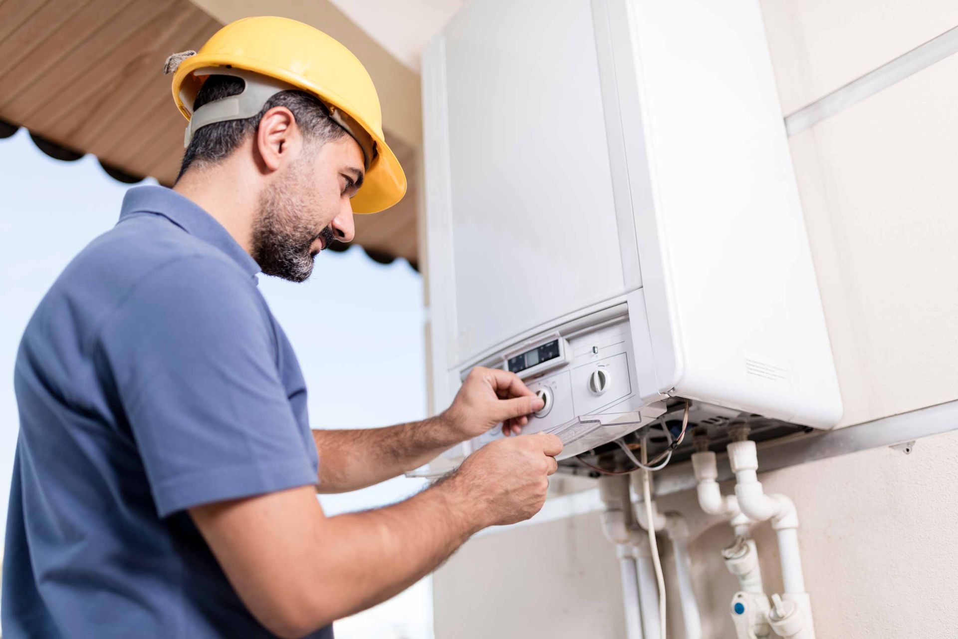 Technician in yellow hard hat adjusting an outdoor wall-mounted boiler or HVAC unit