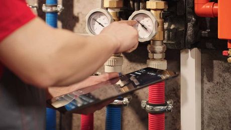 Technician adjusting gauges on plumbing pipes with red and blue hoses in a utility room