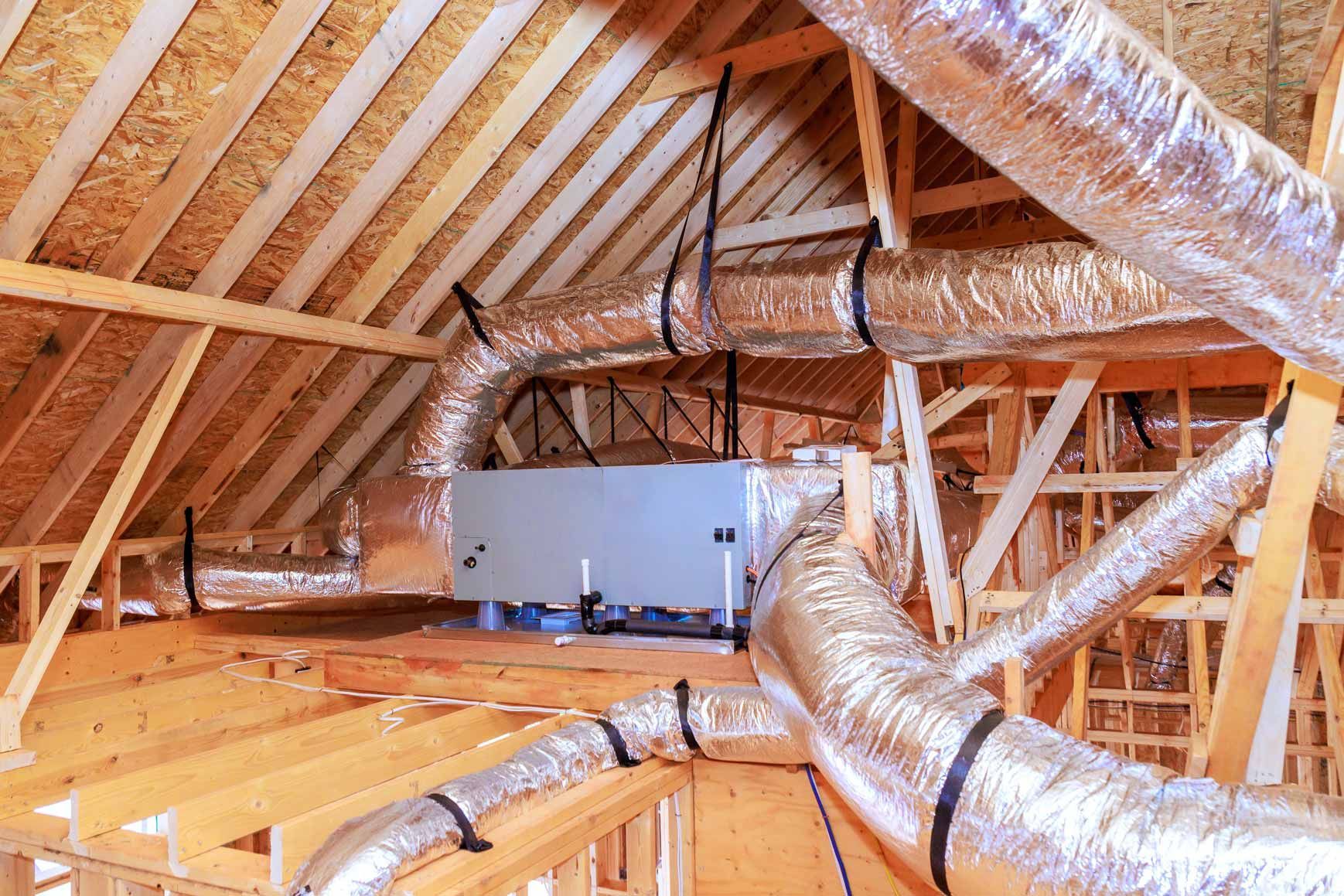 Attic with exposed wooden rafters and shiny silver HVAC ductwork installed overhead
