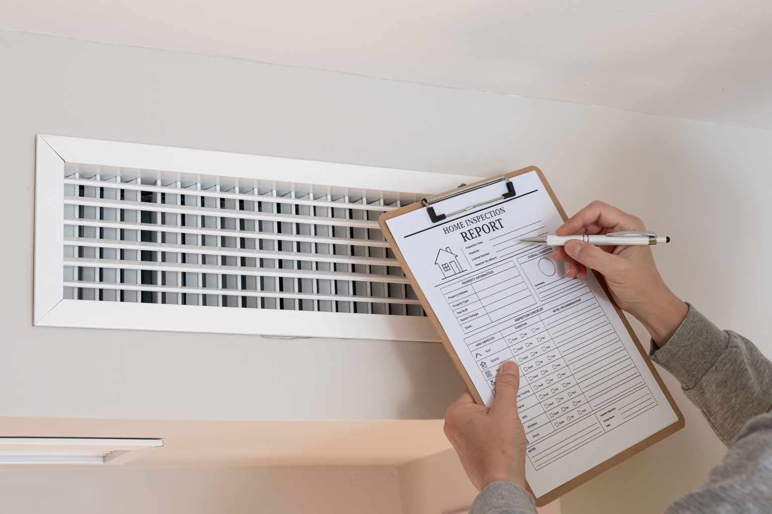 Person writing on a clipboard while inspecting a wall air vent grille