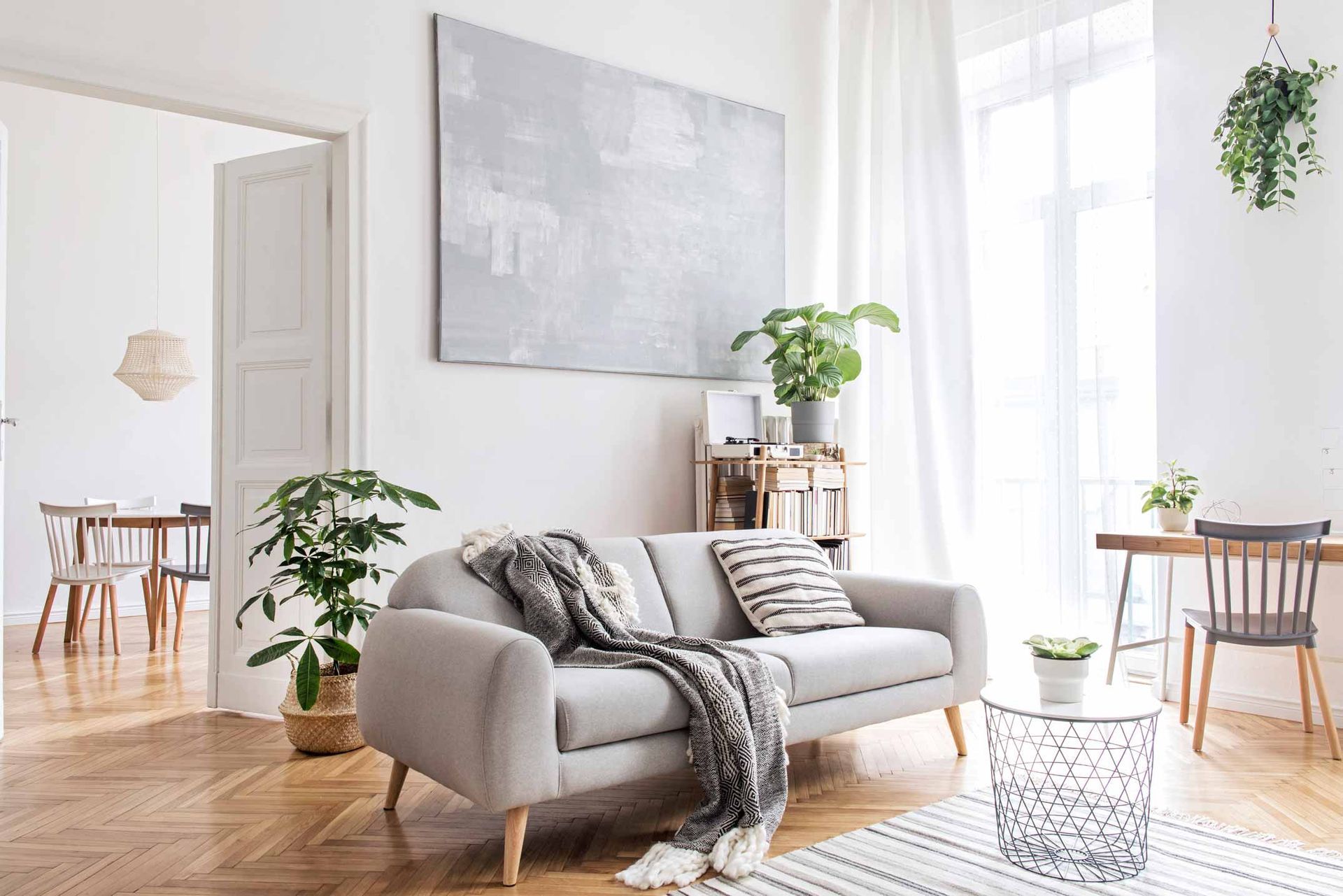 Bright living room with a gray sofa, plants, white decor, and sunlight through large windows