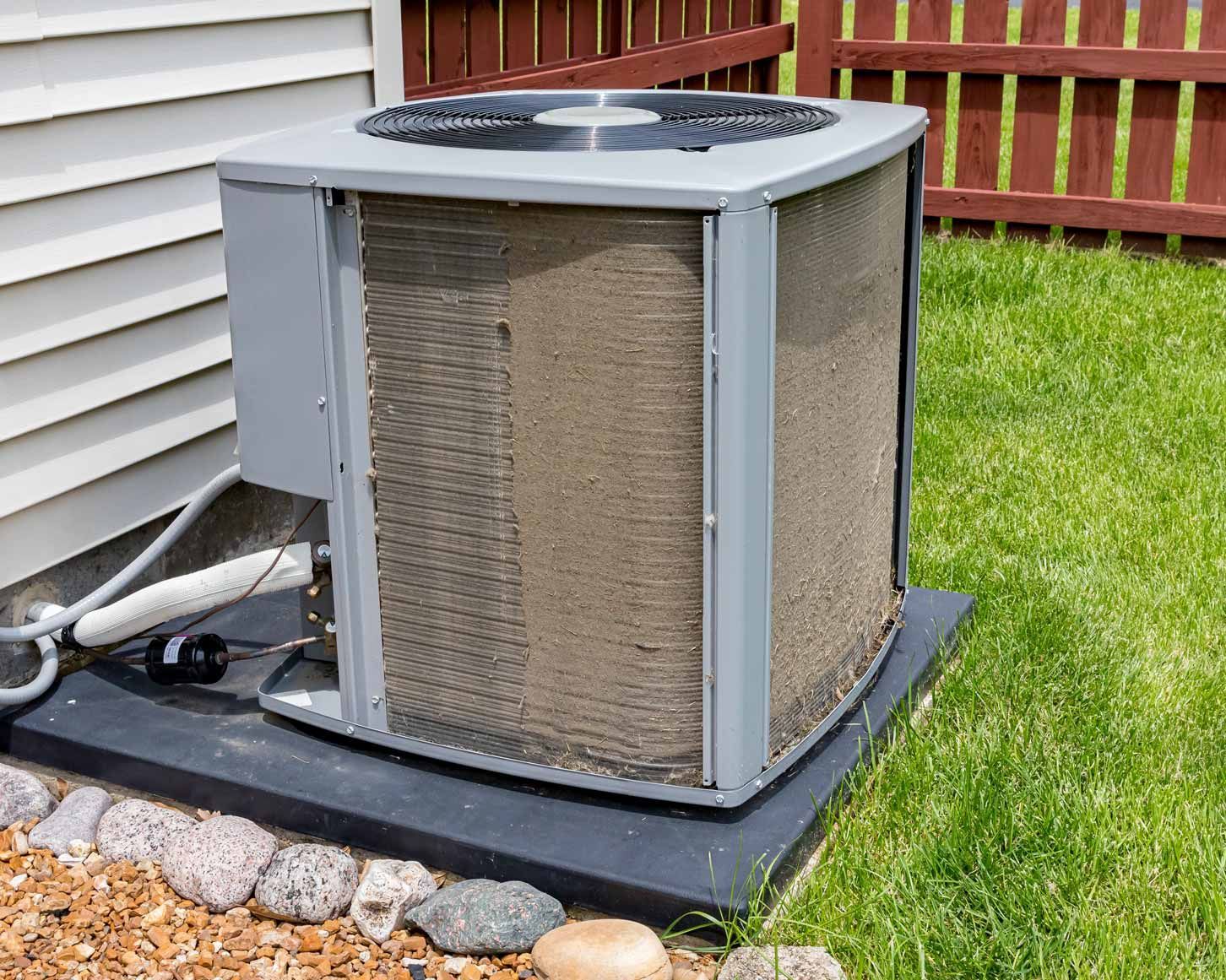 Outdoor air conditioner unit beside a house, on a black pad in a grassy yard