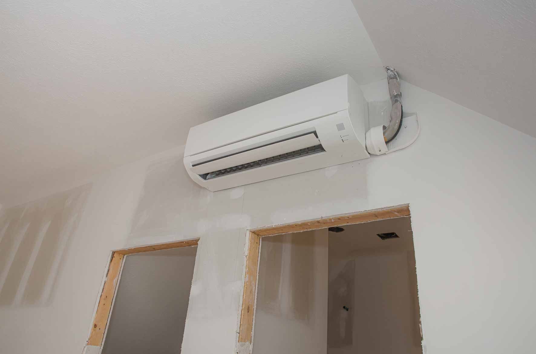 Wall-mounted white air conditioner above two unfinished interior doorways on a white wall