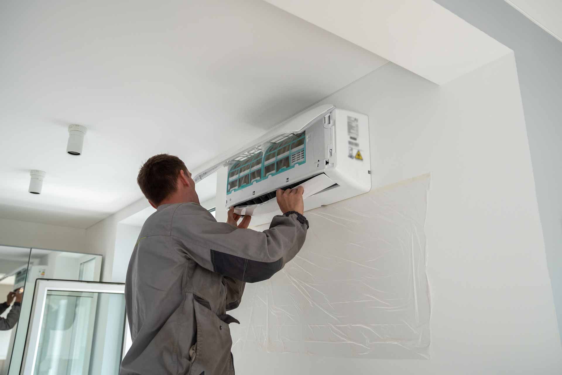 Technician installing a wall-mounted air conditioner in a white room.