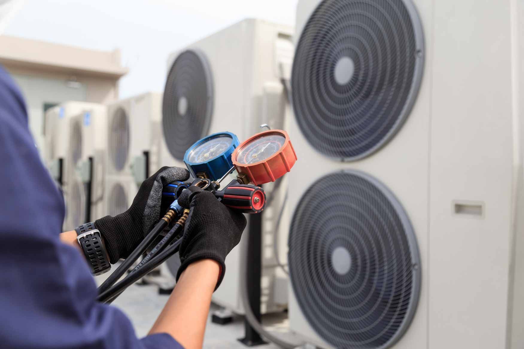 Technician holding manifold gauges to service an outdoor air conditioning unit