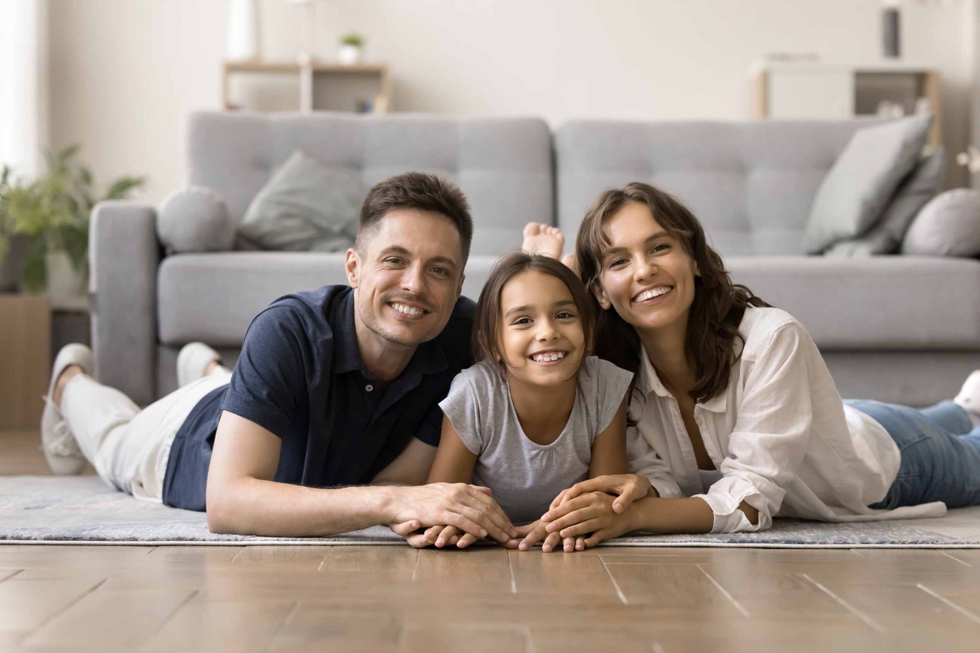 Three people lying on the floor in a bright living room, smiling at the camera.
