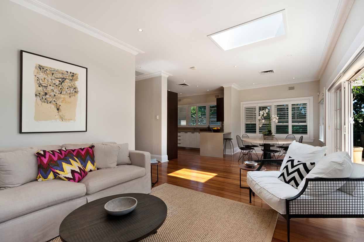 Bright living room with gray sofa, patterned chairs, and large windows in an open-plan home