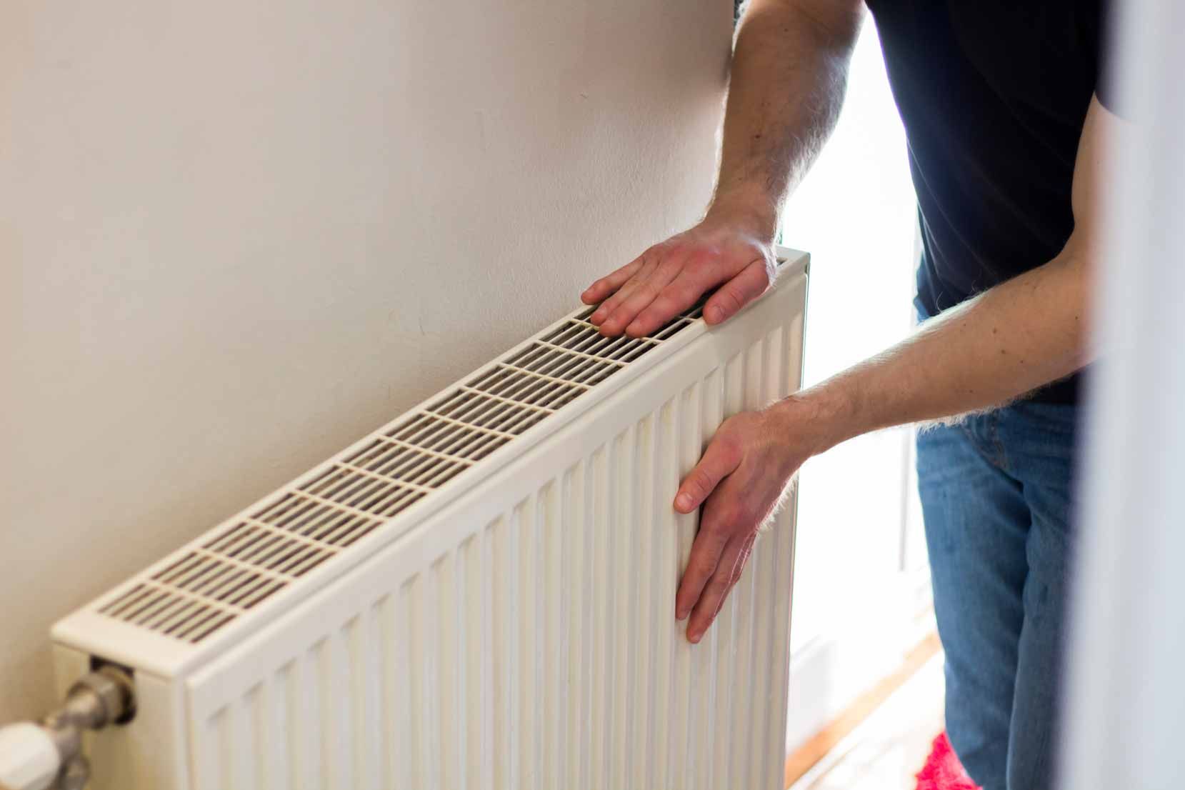 Person installing a white radiator against a wall in a bright room