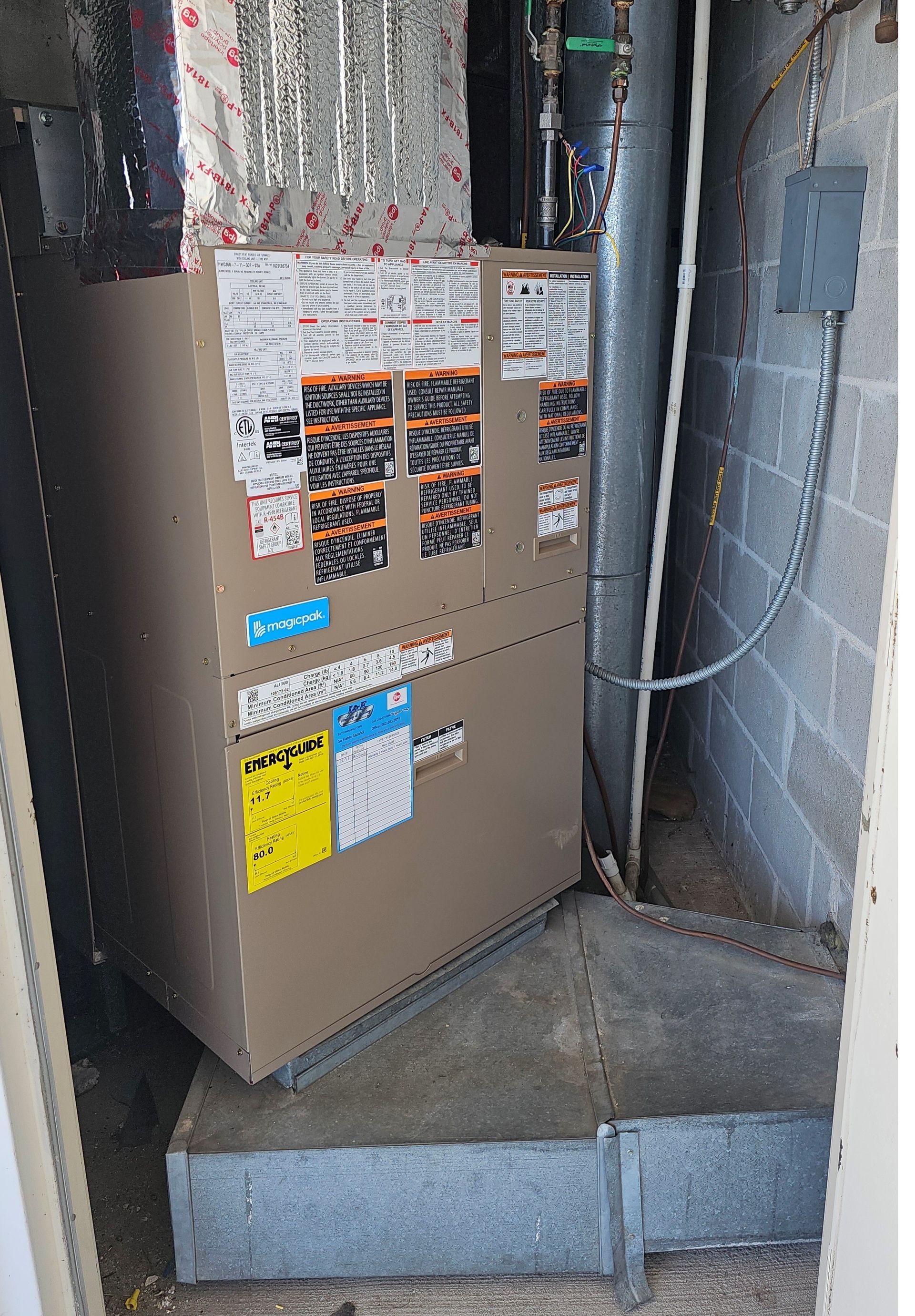 Tan electrical panel in a basement utility area with warning labels and exposed wiring above