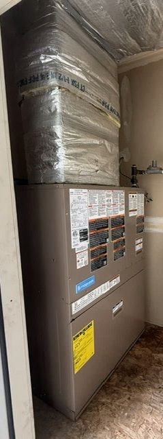 Large HVAC unit in a utility room, with silver ductwork above and a wood floor below.