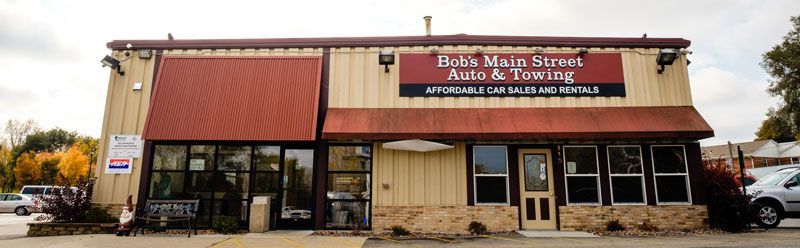 Exterior of a tan storefront with red awnings and a sign for a rural health clinic | Bob's Main Street Auto & Towing