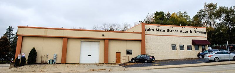 Tan brick auto repair and towing building with parked cars in front | Bob's Main Street Auto & Towing