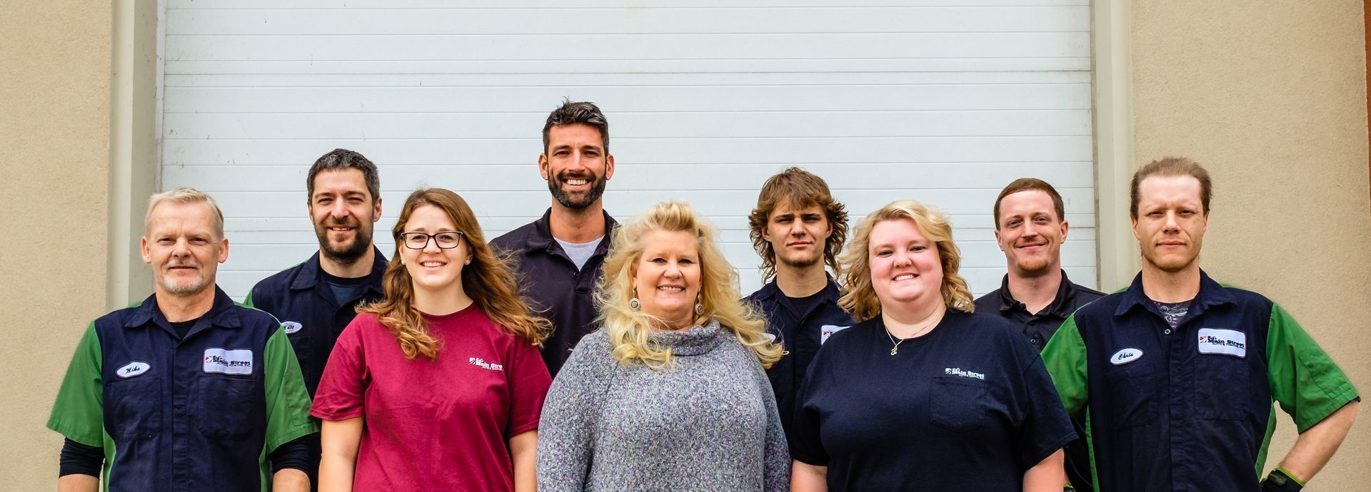 Group of nine people standing together indoors, smiling in matching navy and green shirts | Bob's Main Street Auto & Towing