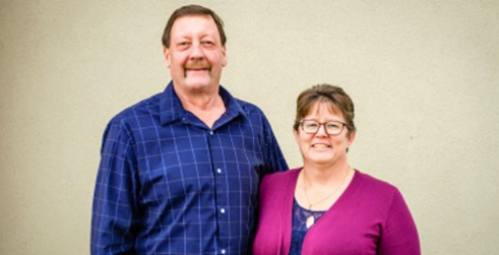 Two people standing side by side, smiling, against a plain beige wall. | Bob's Main Street Auto & Towing