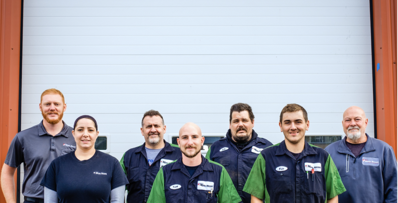 Seven workers stand in front of a large white garage door in a warehouse. | Bob's Main Street Auto & Towing