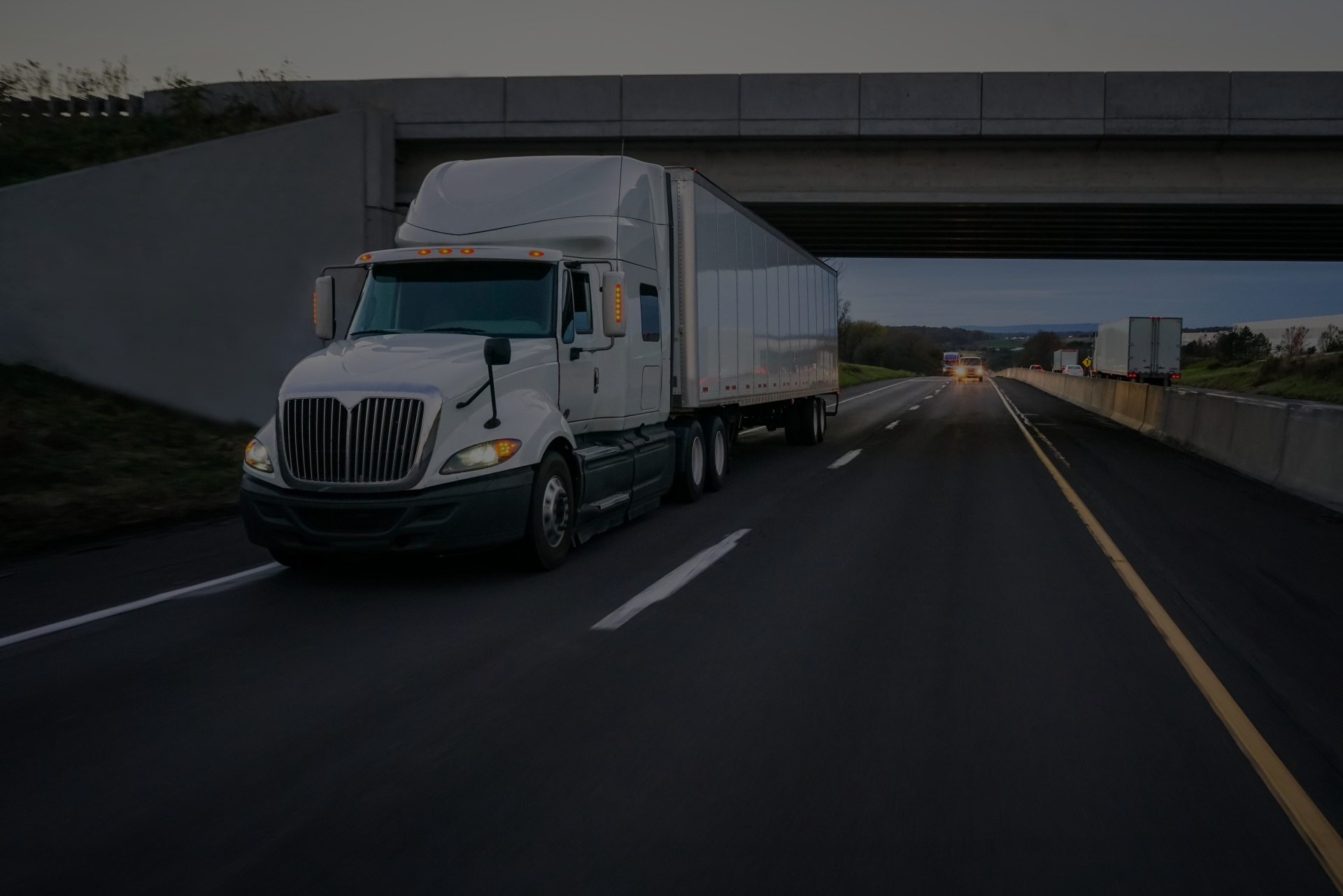 A semi truck is driving down a highway under a bridge.