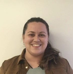 A woman is smiling for the camera while wearing a brown jacket and a blue shirt.